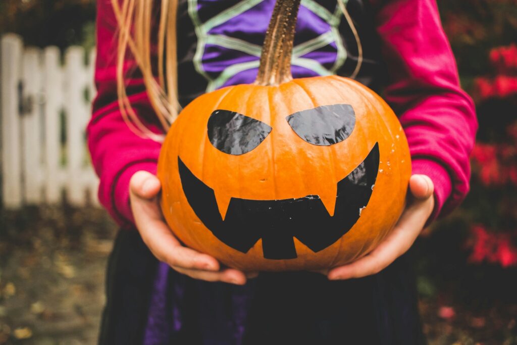 A girl holding a pumpkin with a jack o lantern face painted on it