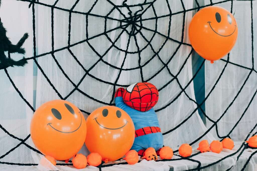A spiderweb backdrop with orange smiley face balloons and a stuffed spiderman toy.